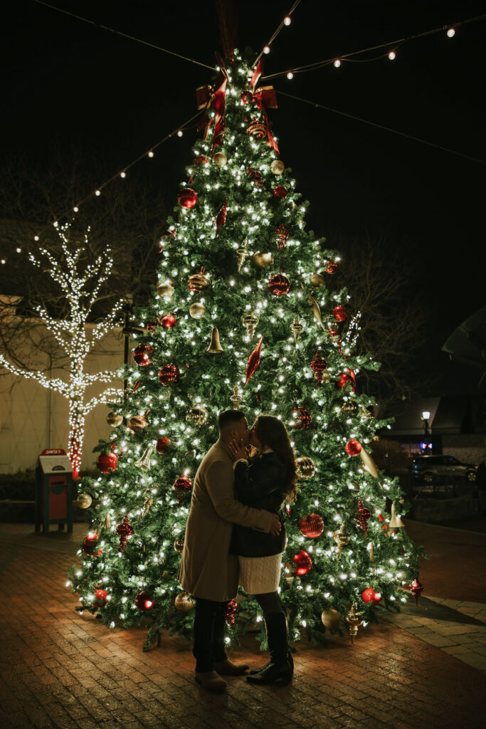 Engaged couple posing under the Christmas lights in Northville’s downtown