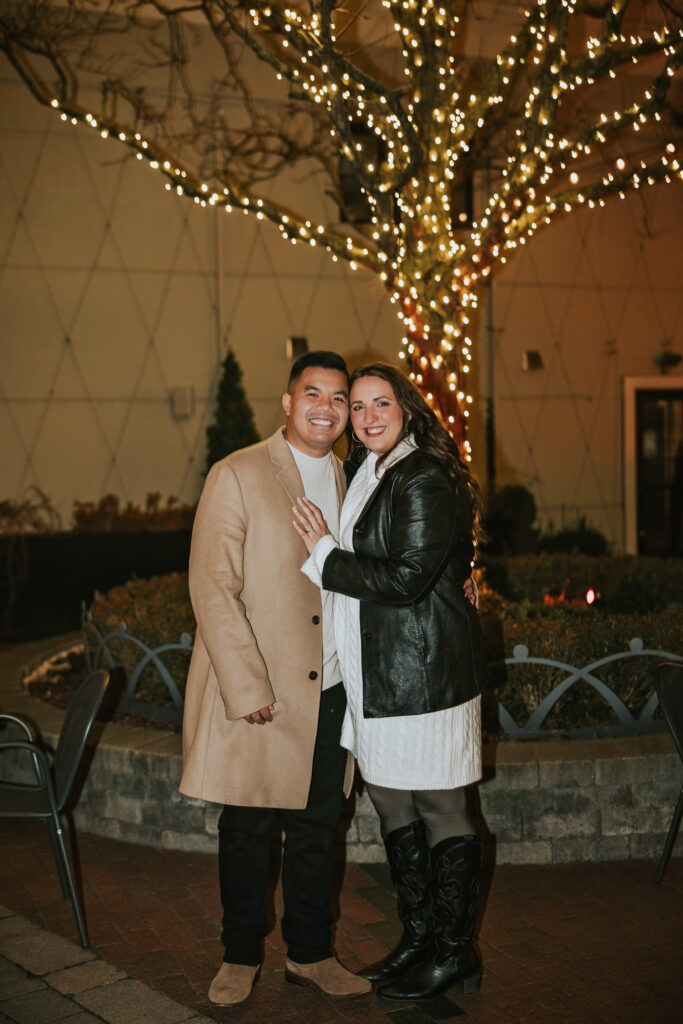 Engaged couple posing under the Christmas lights in Northville’s downtown