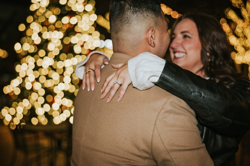 Engaged couple posing under the Christmas lights in Northville’s downtown