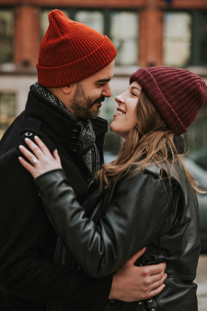 Couple smiling against a snowy Detroit cityscape during their engagement session.