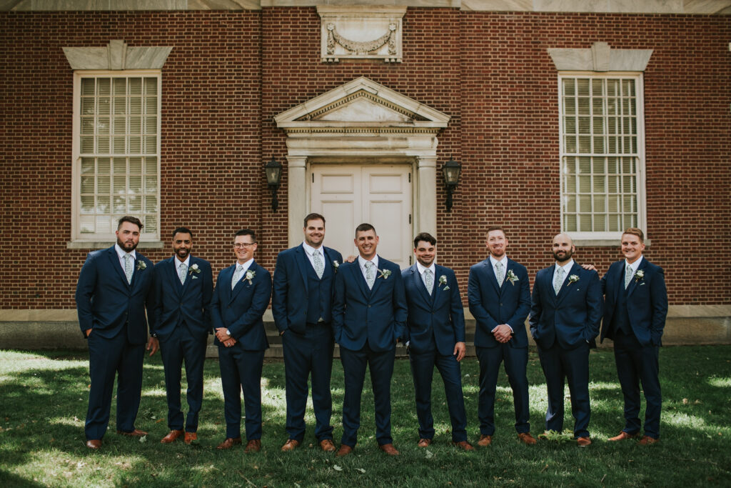 Groom and groomsmen posing outside Lovett Hall for portraits, celebrating a memorable day at Henry Ford Museum.