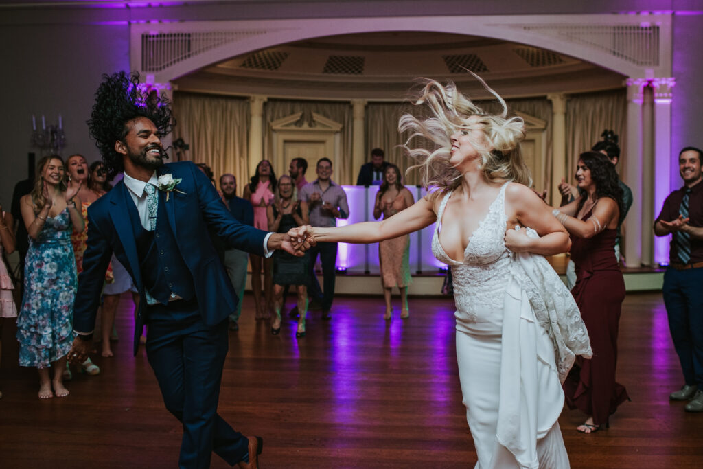 Bride and her friend dancing joyfully at Lovett Hall, Henry Ford Museum, adding fun and excitement to Amanda and Mitchell’s reception.