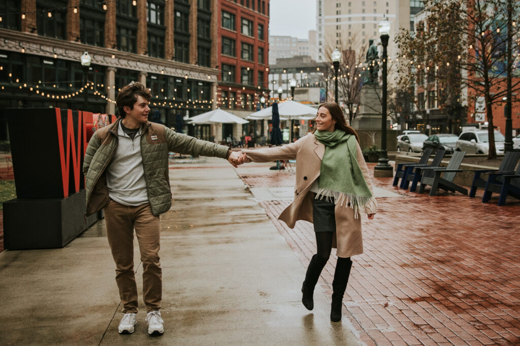 Kate and Tyler walking hand-in-hand through a rainy Detroit street during their engagement session.