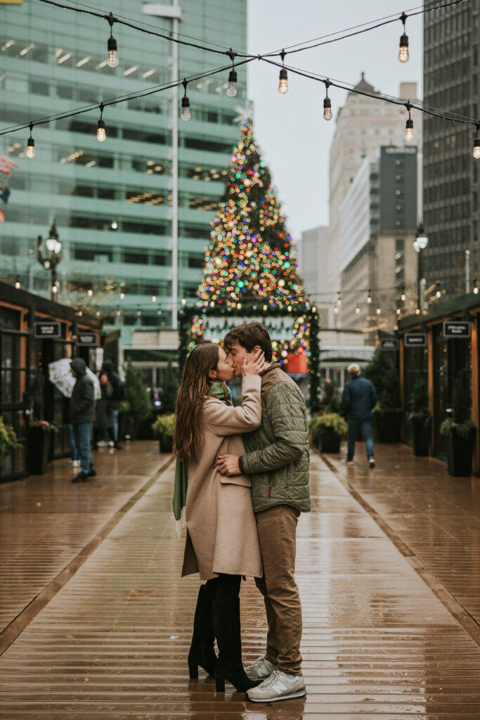 Rainy engagement photo in Cadillac Square, with the Christmas tree lit up behind the couple.