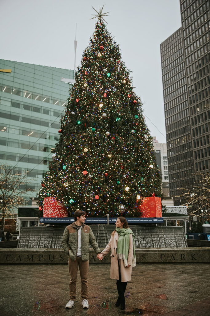 Couple laughing together on a rainy day in Detroit, with Christmas lights in the background.