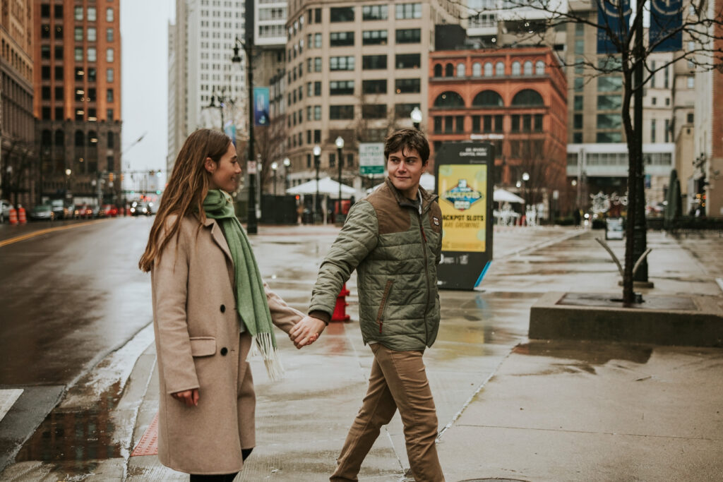 Engagement session at Cadillac Square, Detroit, with couple walking through the rain and city background.