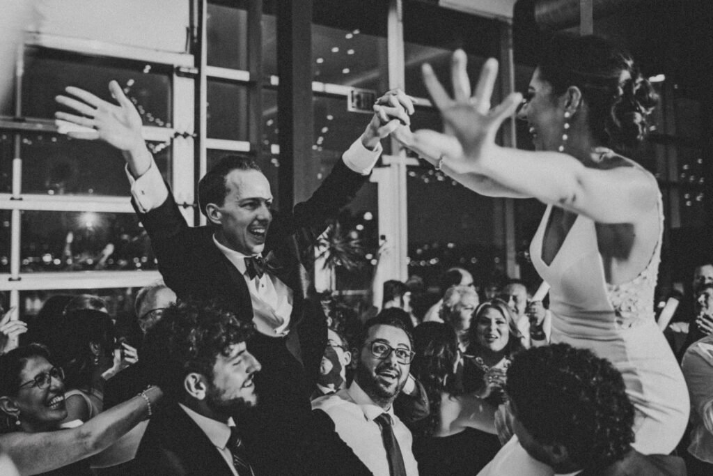 Bride and groom are lifted in the air as part of their dancing celebration at their Waterview Loft Detroit summer wedding.