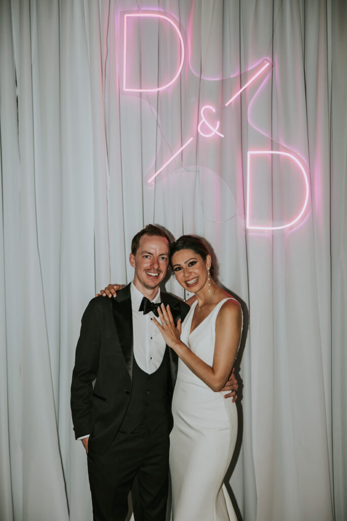 Bride and Groom smile at the camera below their neon sign at their Waterview Loft Detroit wedding reception.