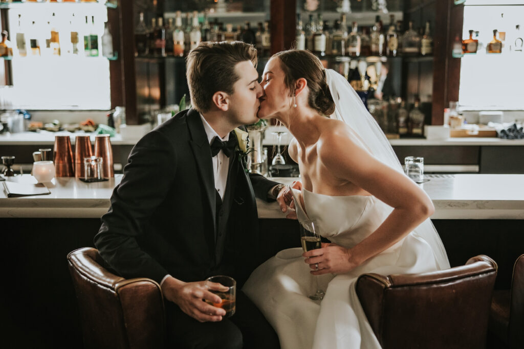 Romantic kiss between bride and groom seated at the bar at the Monarch Club in Detroit | Wedding Planning Tips