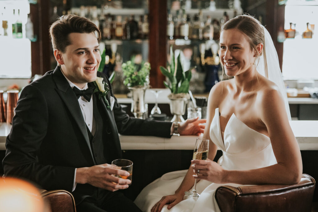 Bride and groom sharing a laugh while sitting at the Monarch Club bar during their wedding day | Wedding Planning Tips