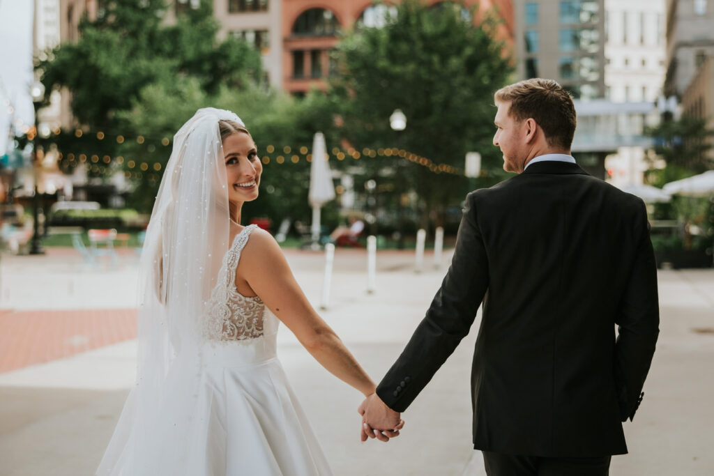 Bride and groom holding hands at Capitol Park with a cityscape backdrop on their wedding day