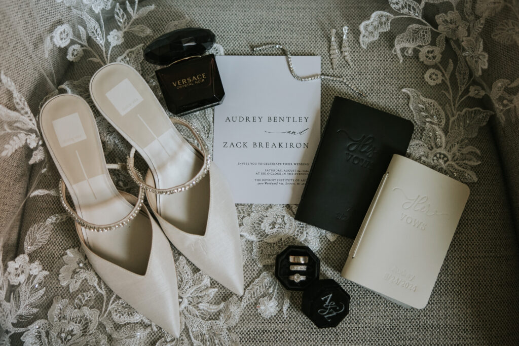 Close-up of intricately detailed wedding shoes, invitation, vow books, and rings