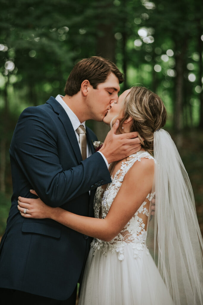 Bride and groom kissing under the old trees, picturesque Traverse City setting.