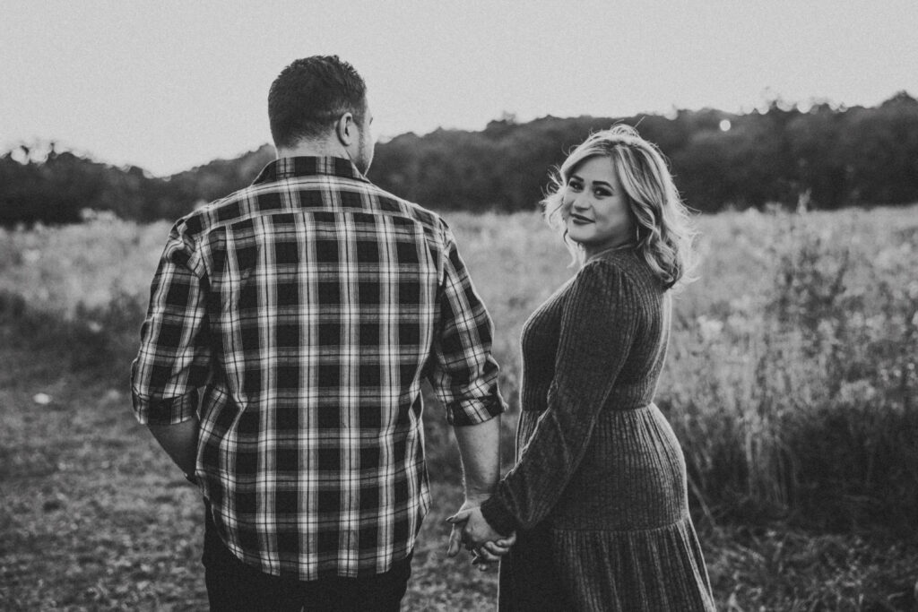 Black and white image of bride looking at the camera as they stroll through the field at their Kensington Metropark Engagement Session